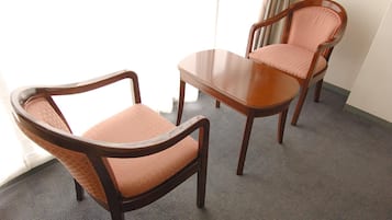 A room with two wooden chairs and a table, carpeted floor, and a window with curtains.