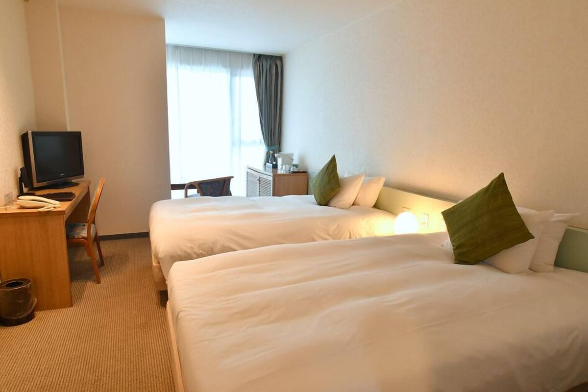 A hotel room with two beds, a desk with a television, and a chair.