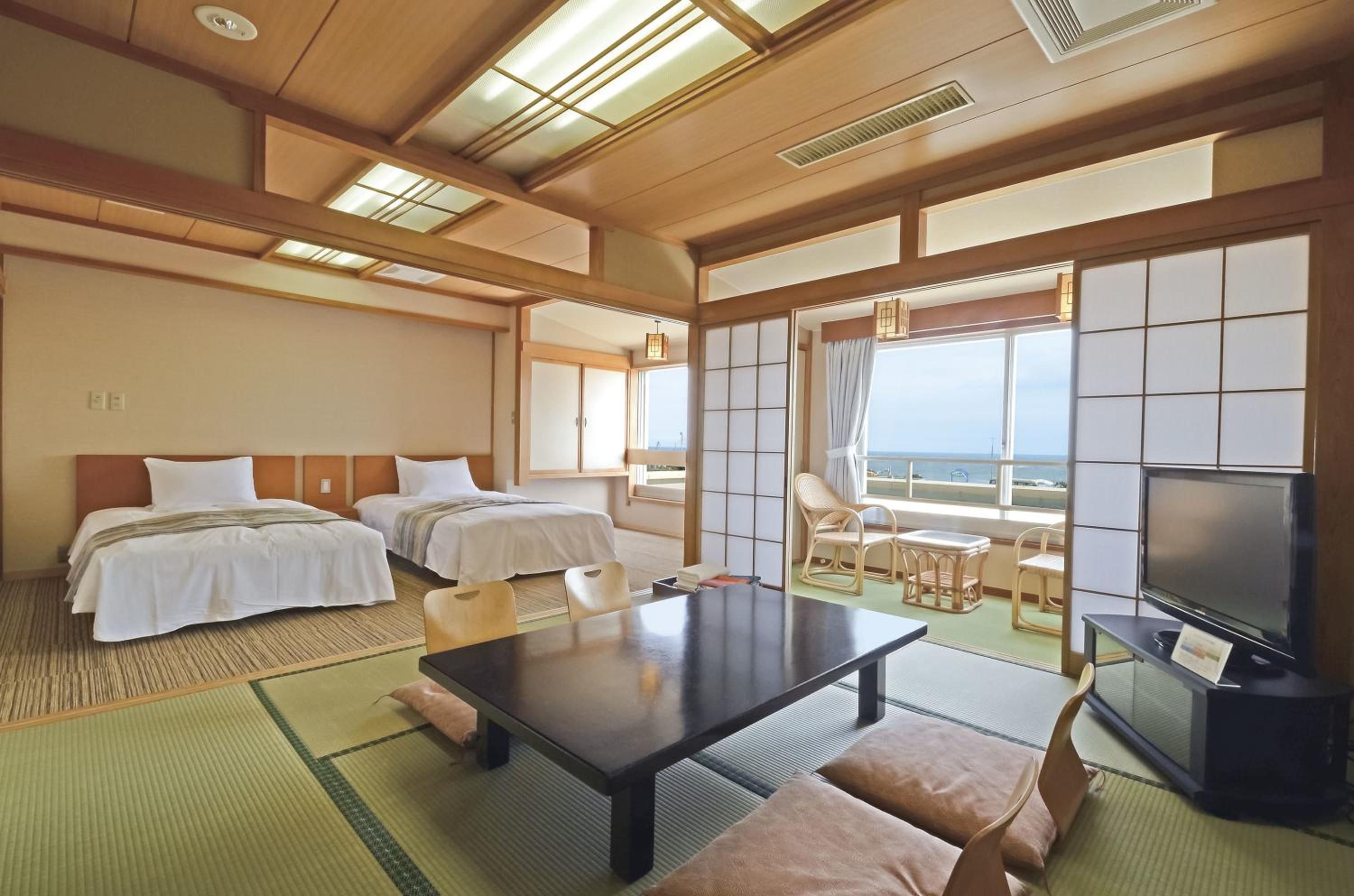 A hotel room with two beds, a dining table, a TV, and a view of the sea.