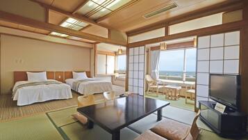 A hotel room with two beds, a dining table, a TV, and a view of the sea.