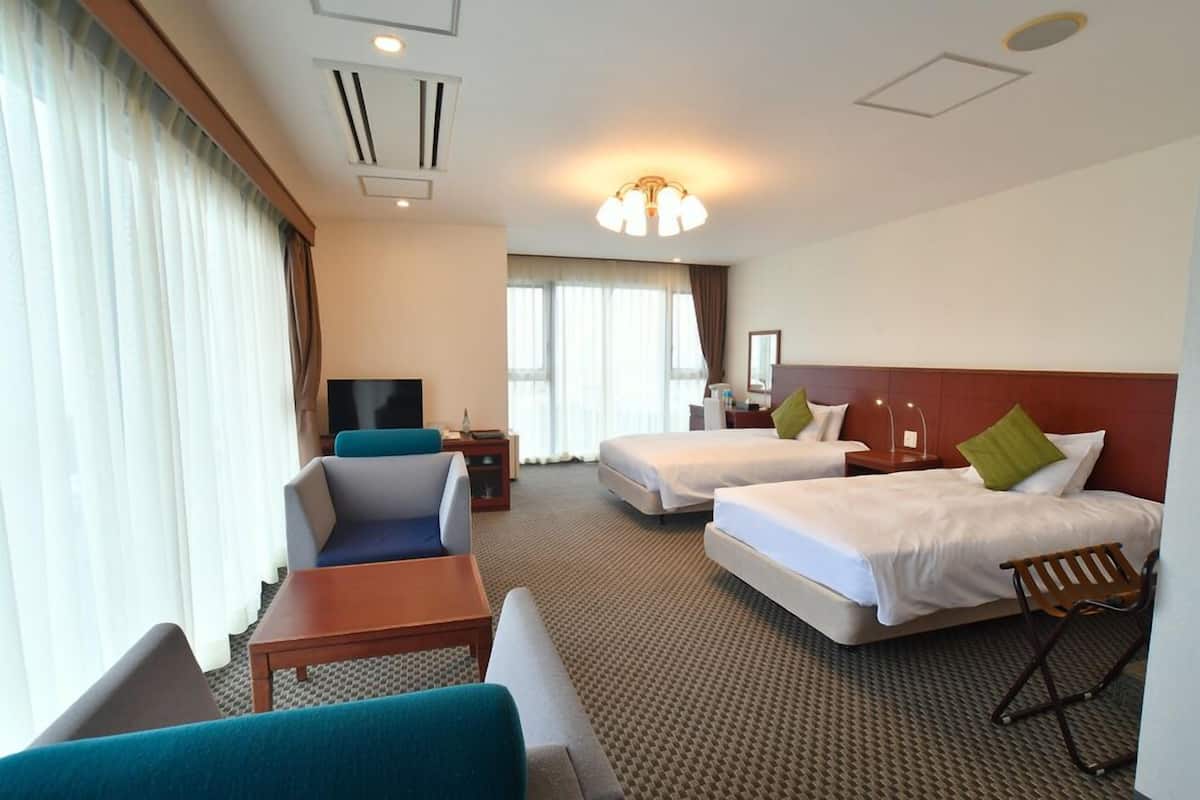 A hotel room with two beds, a sofa, a TV, and a desk.