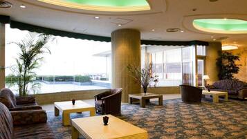 A hotel lobby with seating arrangements, a reception desk, and a view of the outdoors.