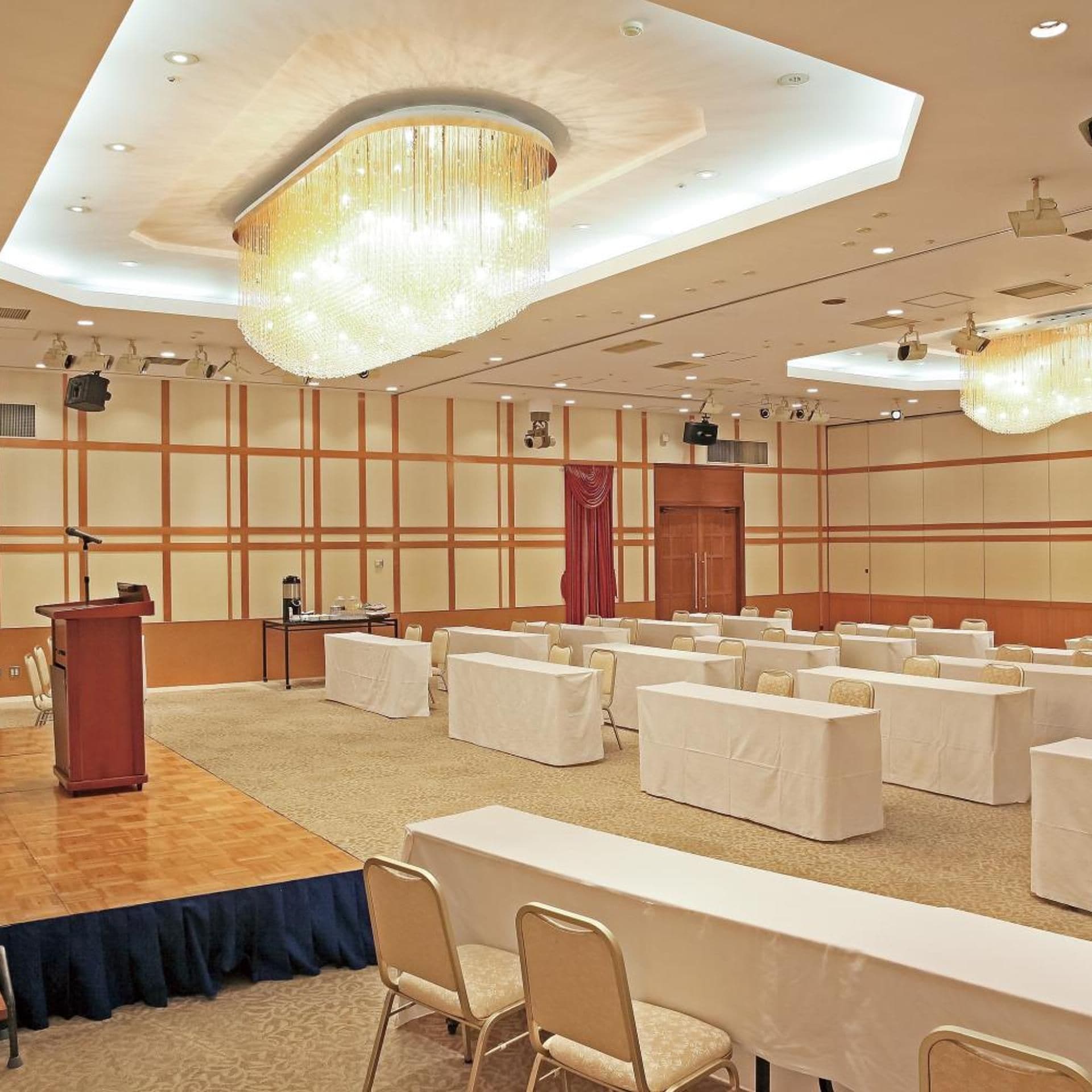 A conference room with a podium, tables, chairs, and a large chandelier.