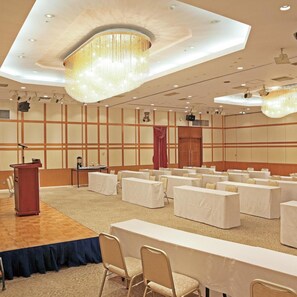 Un salón de conferencias con un atril, mesas, sillas y una gran lámpara de araña.