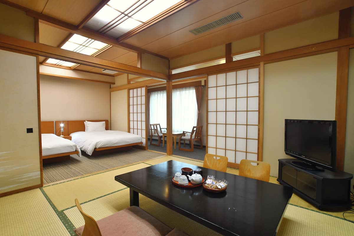 A traditional Japanese room with tatami flooring, a low table with tea set, a bed with white bedding, and a television on a stand.