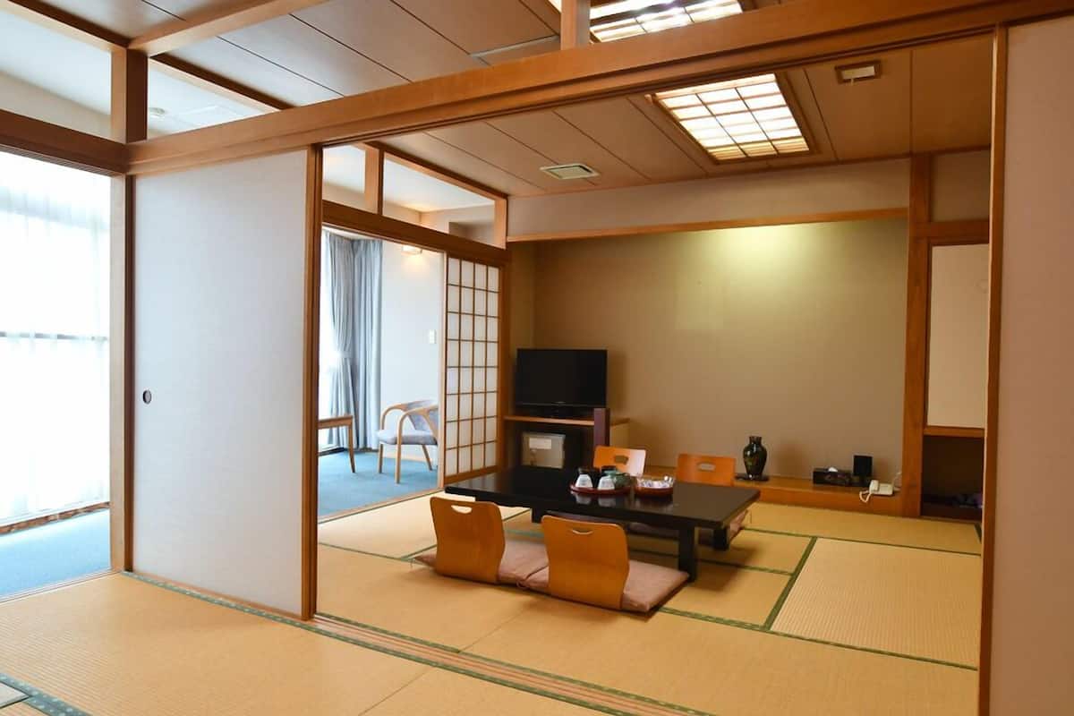 A traditional Japanese-style room with tatami flooring, a low table with cushions, a television, and sliding doors.