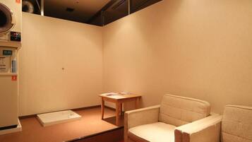 A room with a red carpet, a wooden table, two chairs, and a white appliance on the left.
