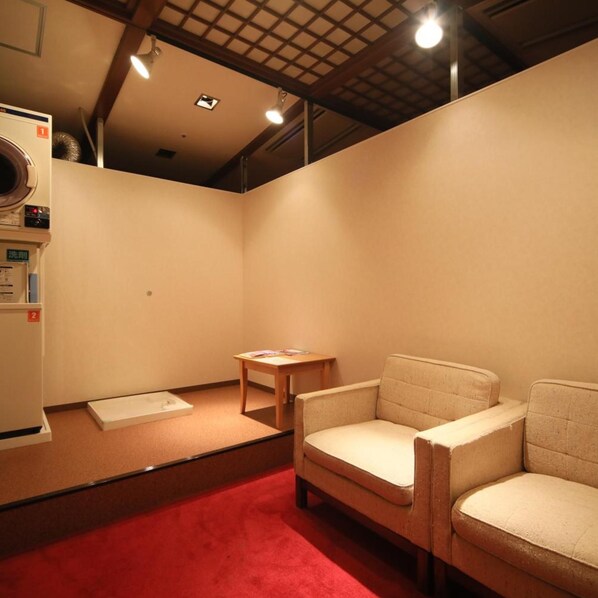 Una habitación con alfombra roja, una mesa de madera, dos sillas y un electrodoméstico blanco a la izquierda.