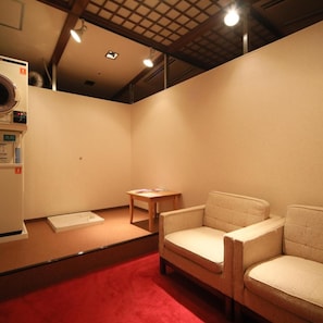A room with a red carpet, a wooden table, two chairs, and a white appliance on the left.