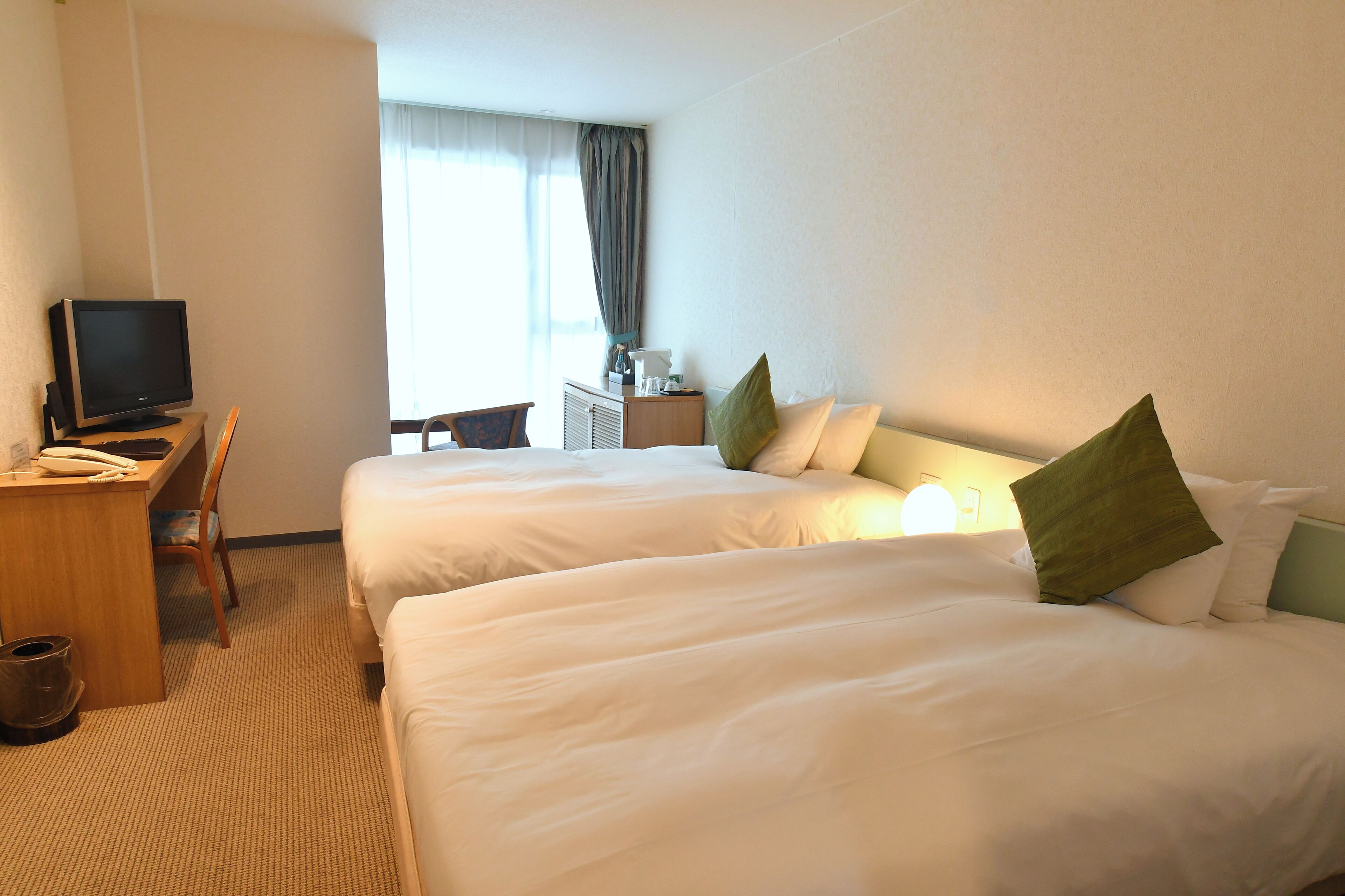 A hotel room with two beds, a desk with a computer, and a chair.