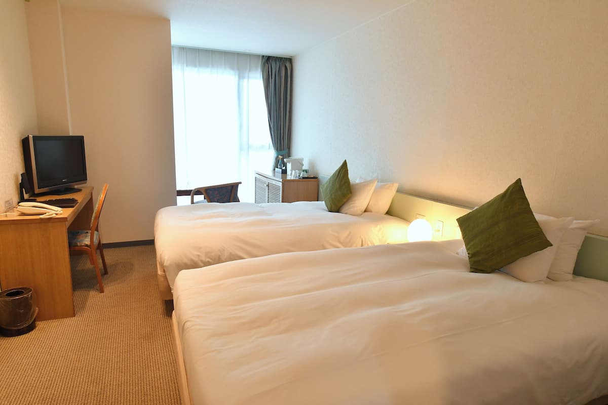 A hotel room with two beds, a desk with a computer, and a chair.