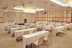 Ein Konferenzraum mit Reihen von Tischen und Stühlen, einer Bühne mit Vorhängen und einer Kristallleuchtre.