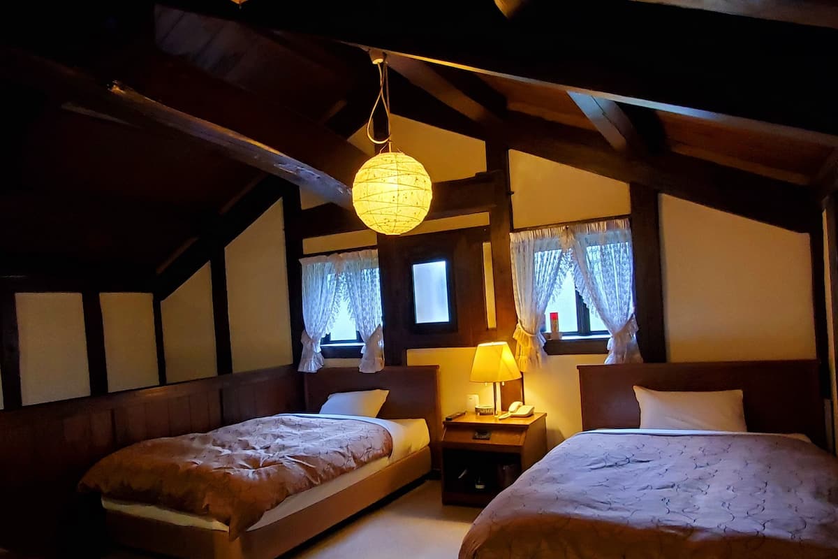 A cozy room with two beds, a hanging light fixture, a nightstand, and a window with curtains.