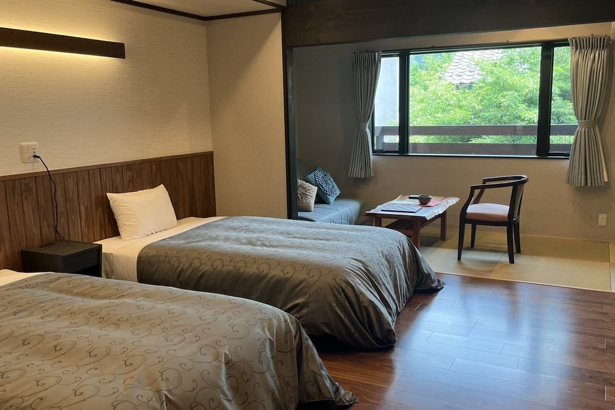 A hotel room with two beds, a small table, a chair, and a window with curtains.