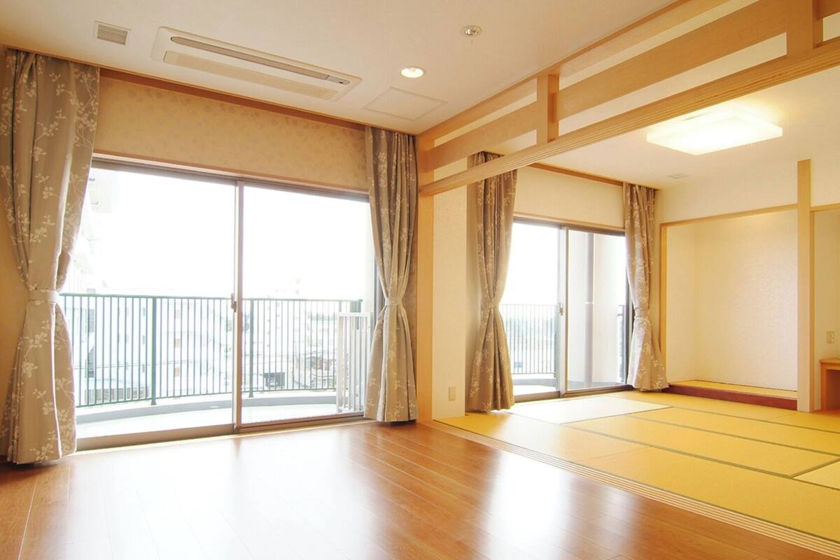 Una habitación con grandes puertas correderas de vidrio, suelo de madera y una zona con esteras de tatami.