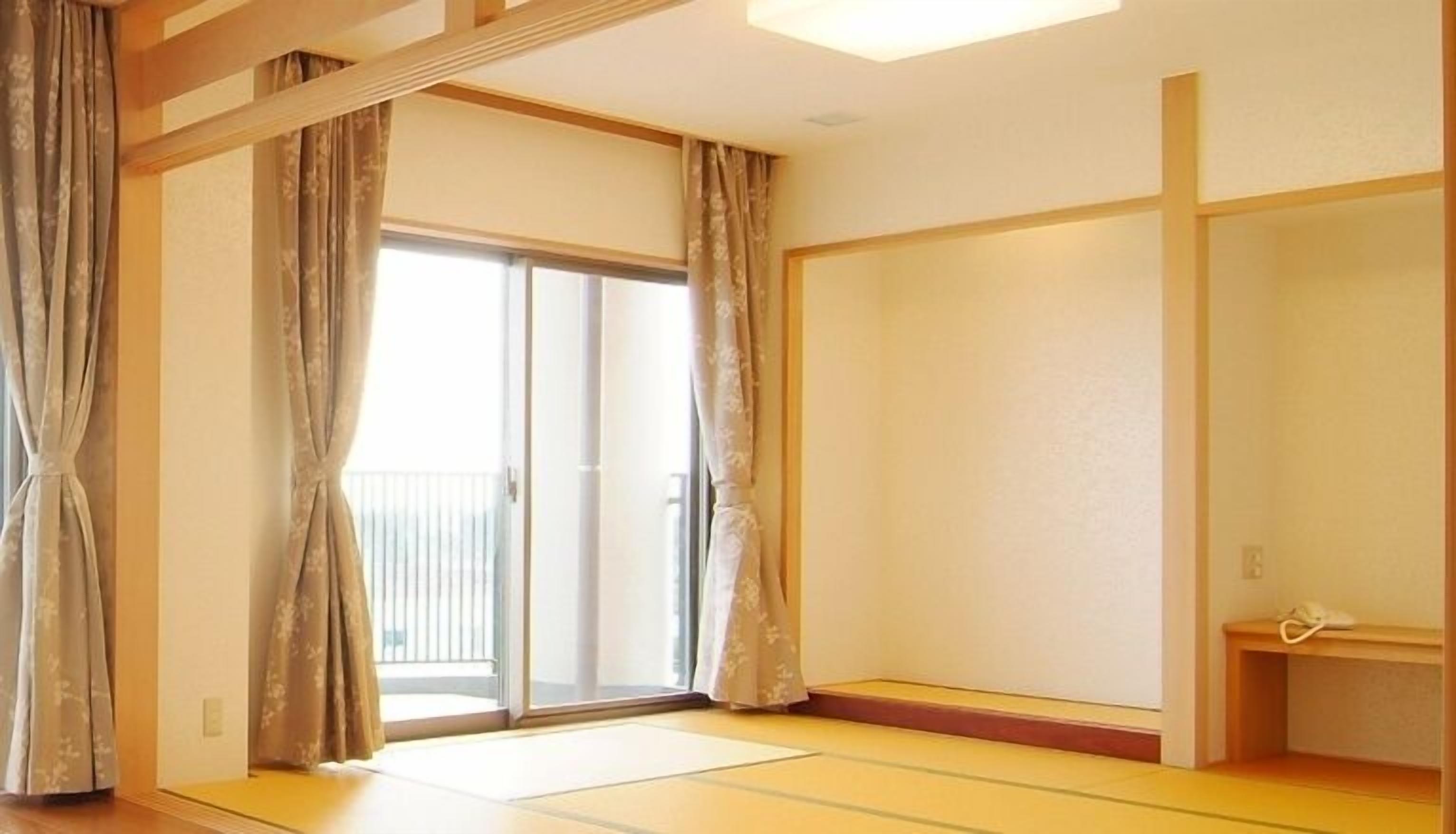 Ein Zimmer mit Tatami-Böden, Schiebetüren, einem kleinen Regal und einer Leuchte.