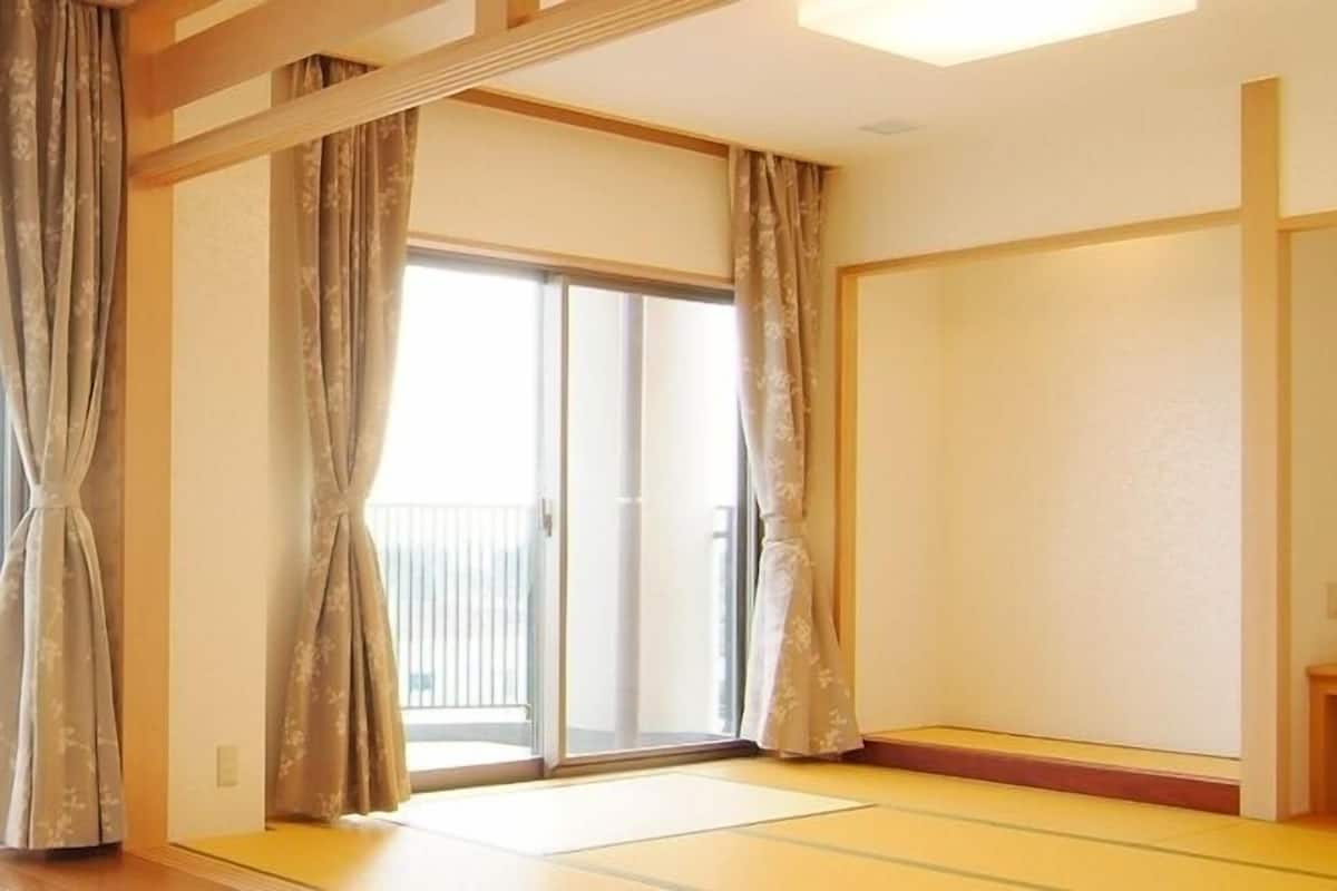 Una habitación con suelo de tatami, puertas correderas, un estante pequeño y una lámpara.
