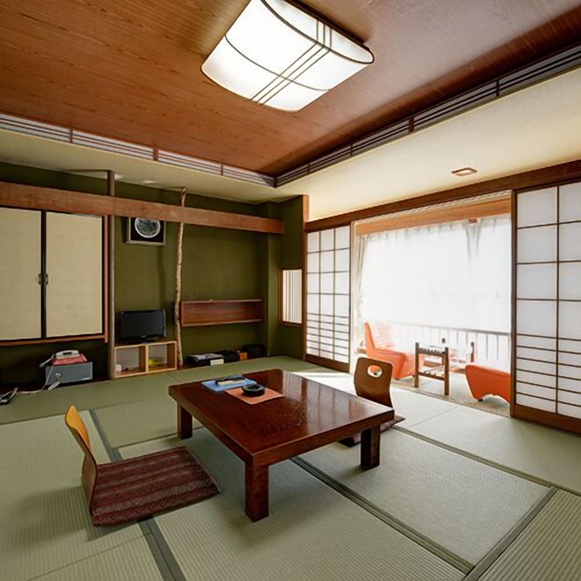 Una habitación japonesa tradicional con suelo de tatami, una mesa de madera baja, un televisor y puertas correderas.