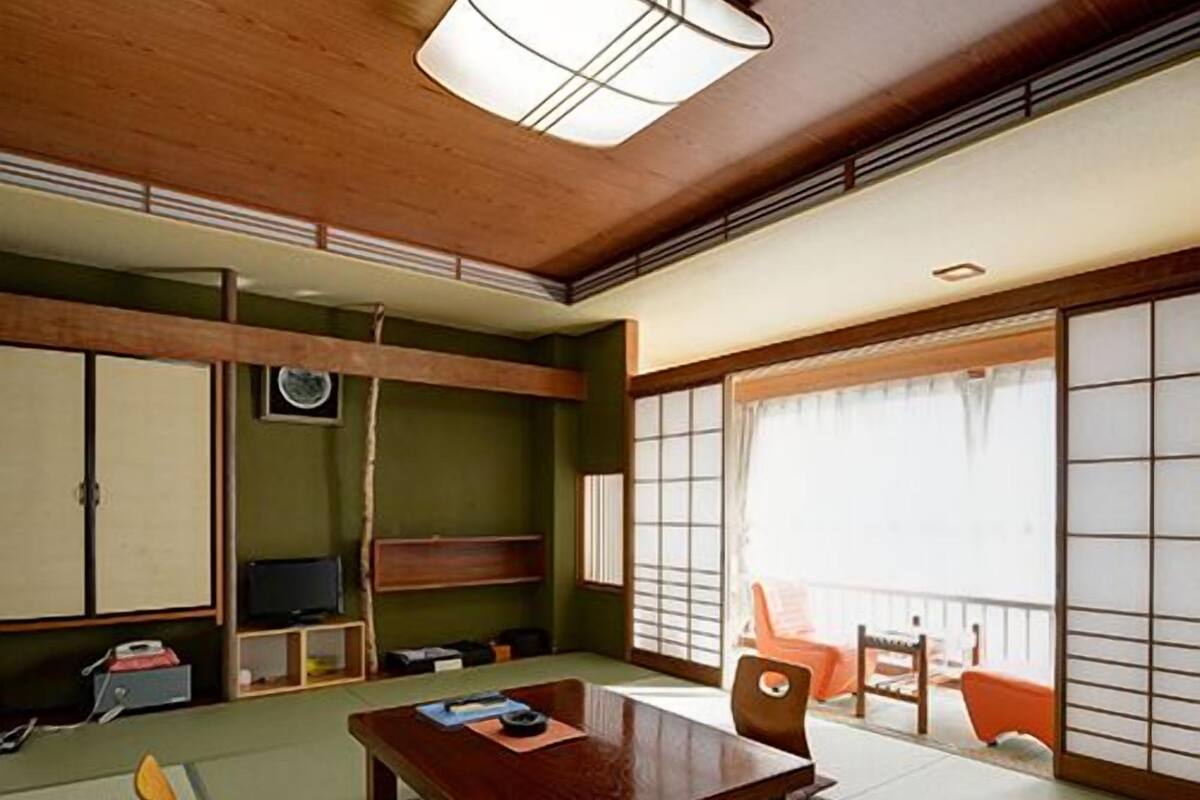Ein traditioneller japanischer Raum mit Tatami-Boden, einem niedrigen Holztisch, einem Fernseher und verschiebbaren Türen.