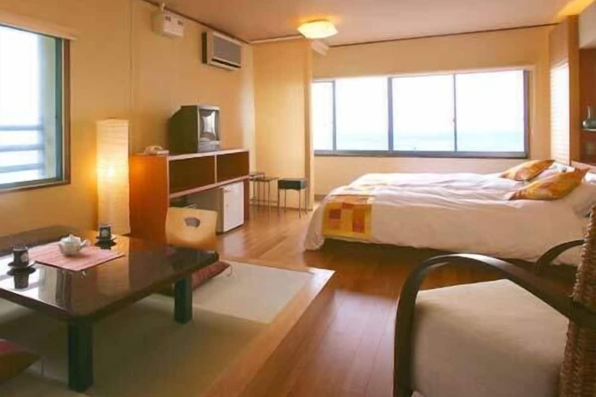 Ein Hotelzimmer mit Bett, Schreibtisch, Stuhl, kleinem Tisch, Fernseher und Fenster.