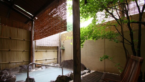 Un onsen japonés tradicional con un banco de madera, una bañera de piedra y paredes de bambú.