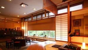 Una habitación japonesa tradicional con suelo de tatami, una mesa baja con cojines, un juego de té y vistas a través de biombos shoji.