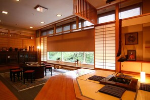 A traditional Japanese room with tatami flooring, a low table with cushions, a tea set, and a view through shoji screens.