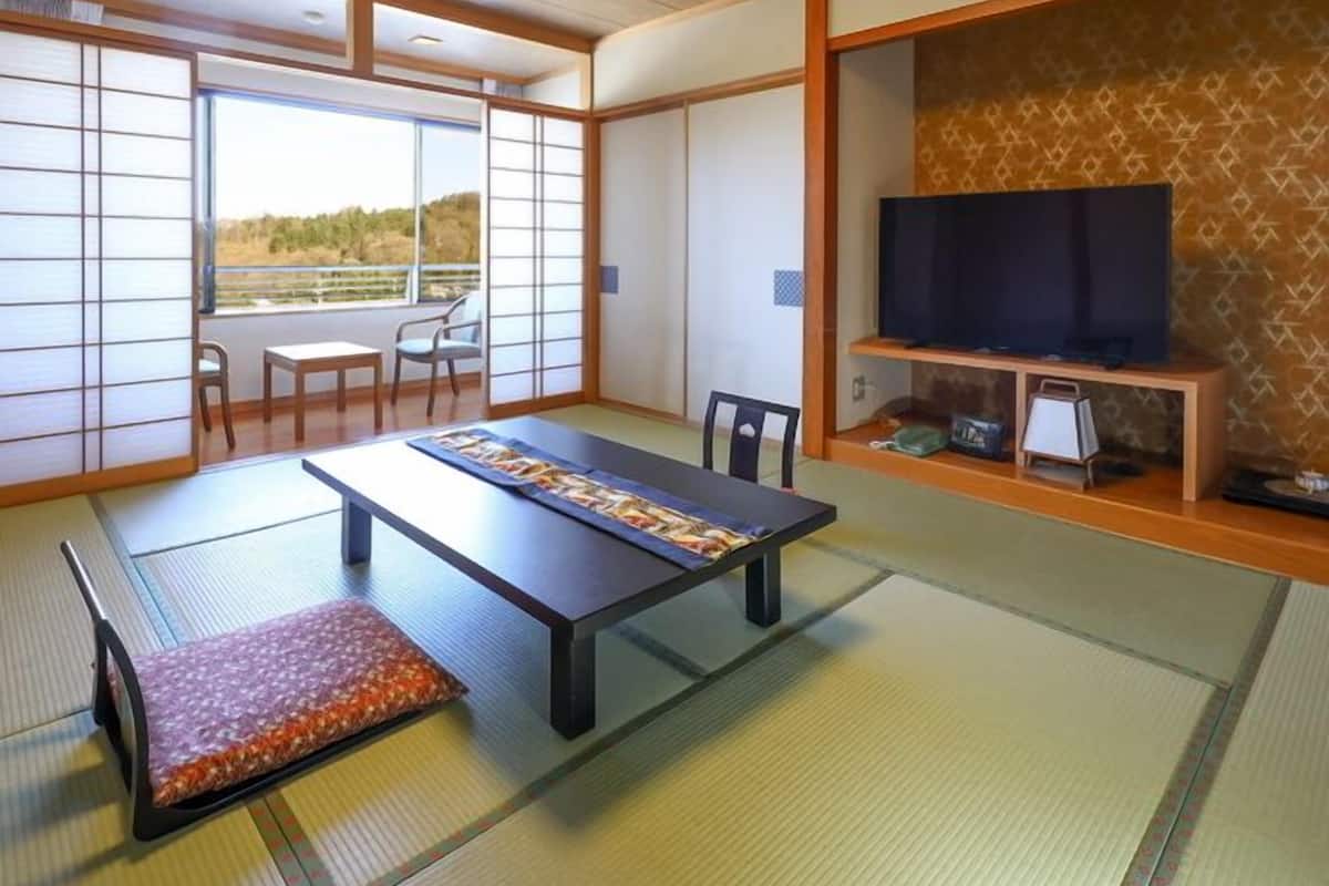 Habitació amb tatamis i una taula de tatami, televisió sobre un prestatge de fusta i vista a través d'una pantalla shoji.