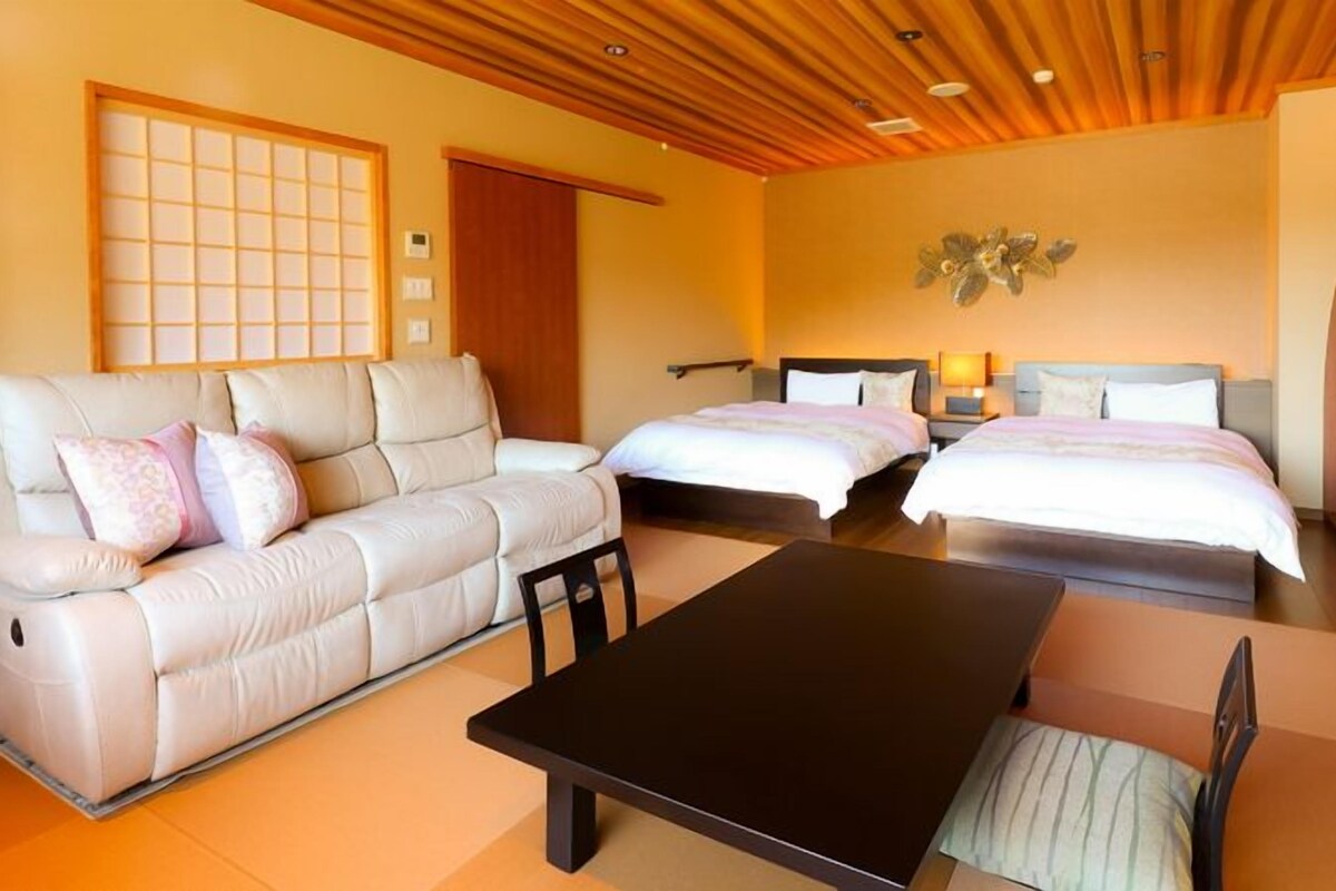 A hotel room with a sofa, two beds, a table, and a decorative wall piece.