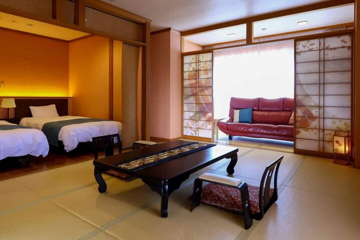 Habitació d'hotel d'estil japonès tradicional amb fusteria de tatami, dos llits, una taula baixa i un sofà vermell.