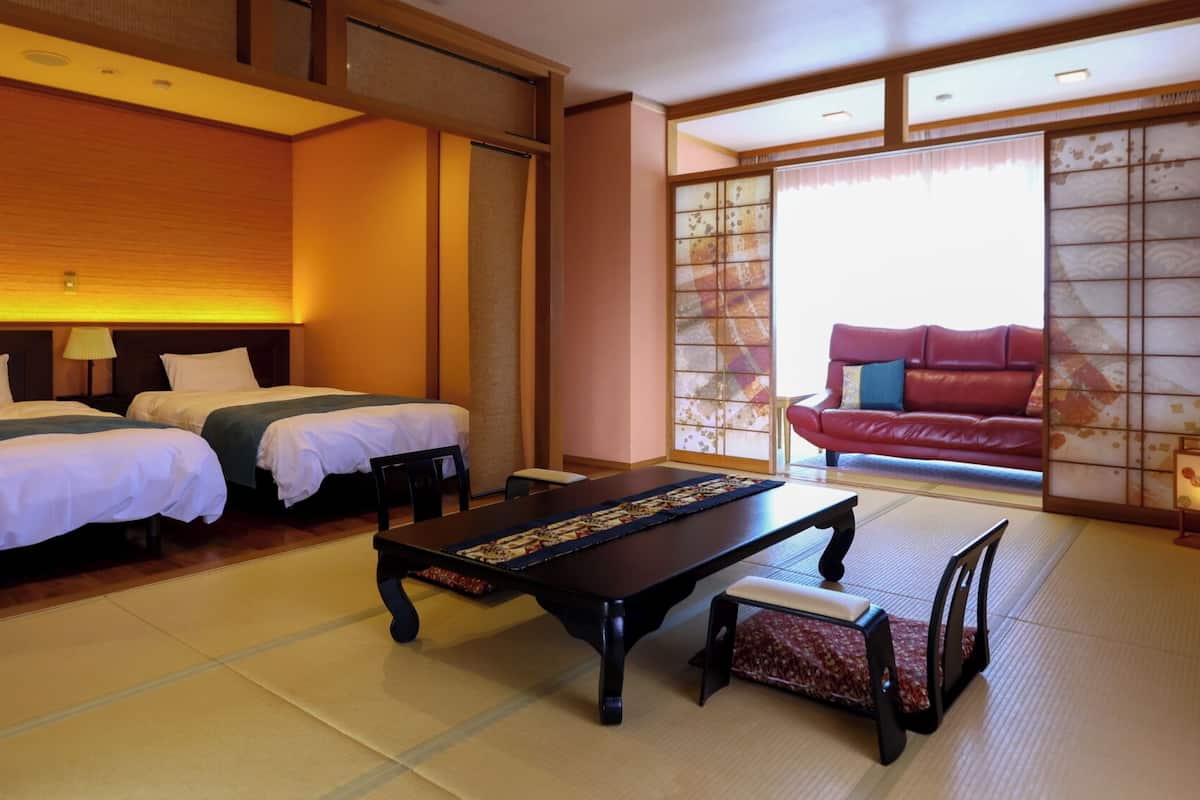 Habitació d'hotel d'estil japonès tradicional amb sòls de tatami, dos llits, una taula baixa i un sofà vermell.