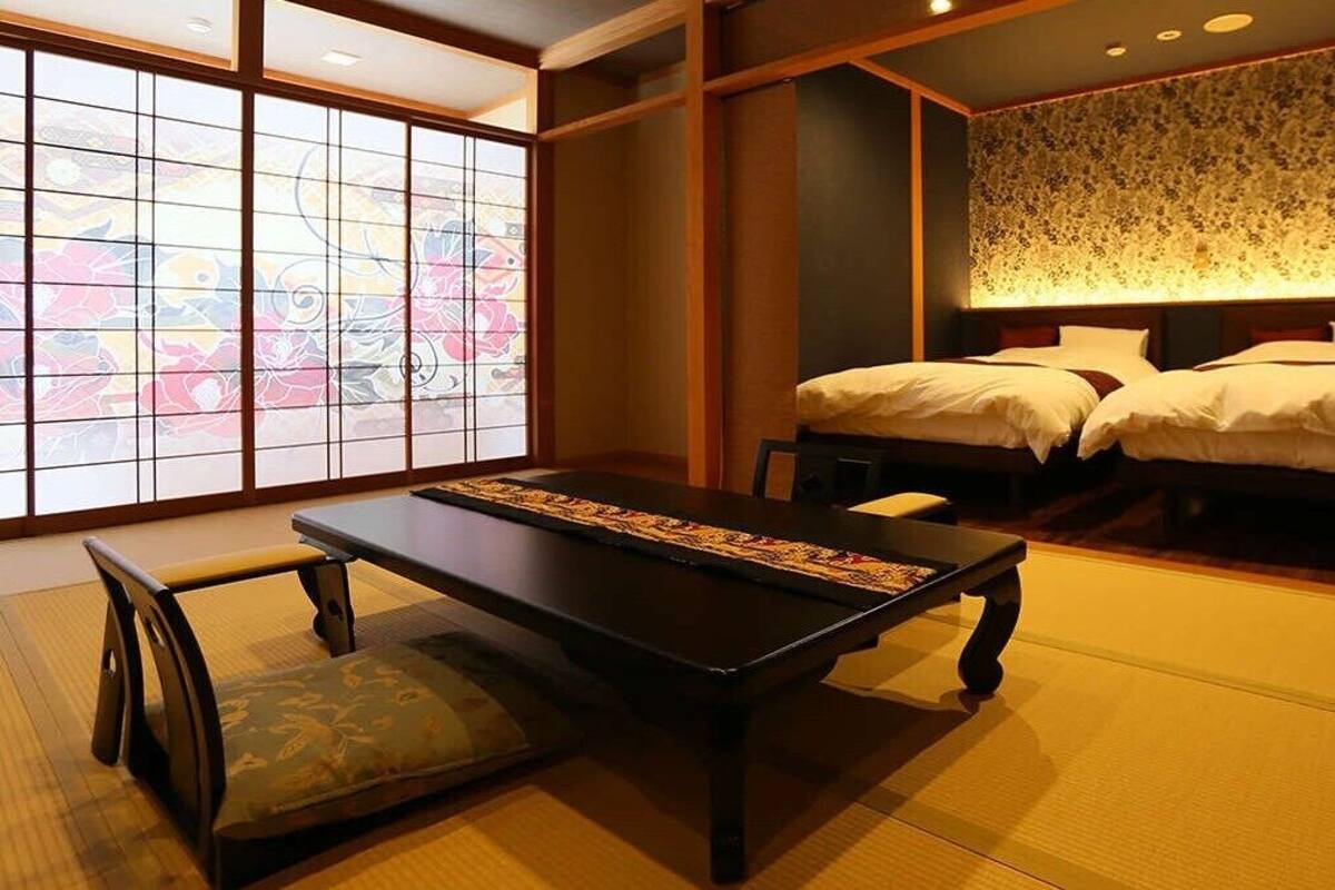 Habitació japonesa tradicional amb terra de tatami, una taula baixa amb coixins i un llit amb capçaleri de flors.
