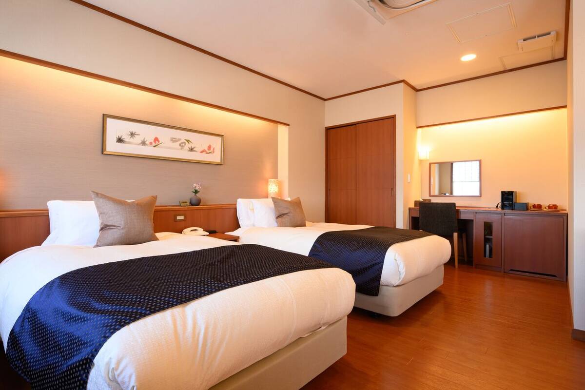 A hotel room with two beds, a desk, a mirror, and a framed picture on the wall.