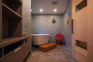A bathroom with a bathtub, a wooden bench, a red chair, and a shelf with a bowl. - Hotel Meguma (Wakkanai)