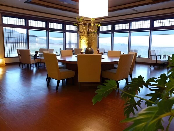 A conference room with a round table, chairs, and large windows with a view. - Hotel Meguma (Wakkanai)
