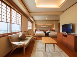 A hotel room with a sofa, two beds, a TV, and large windows. - Hotel Meguma (Wakkanai)