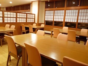 A conference room with multiple tables and chairs, large windows with traditional wooden frames, and a modern ceiling design. - Hotel Meguma (Wakkanai)