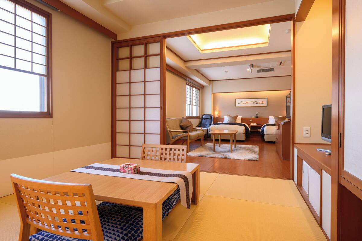 A traditional Japanese-style room with tatami flooring, a low table with a cushion, a wooden chair, and a sliding door.