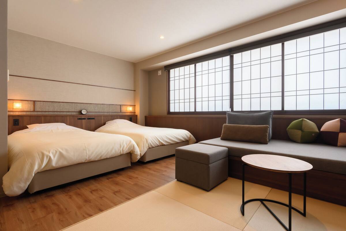 A hotel room with two beds, a sofa, a small table, and a large window.