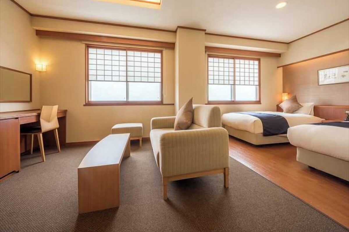 Una habitación de hotel con un escritorio, dos sofás, un banco y ventanas amplias.
