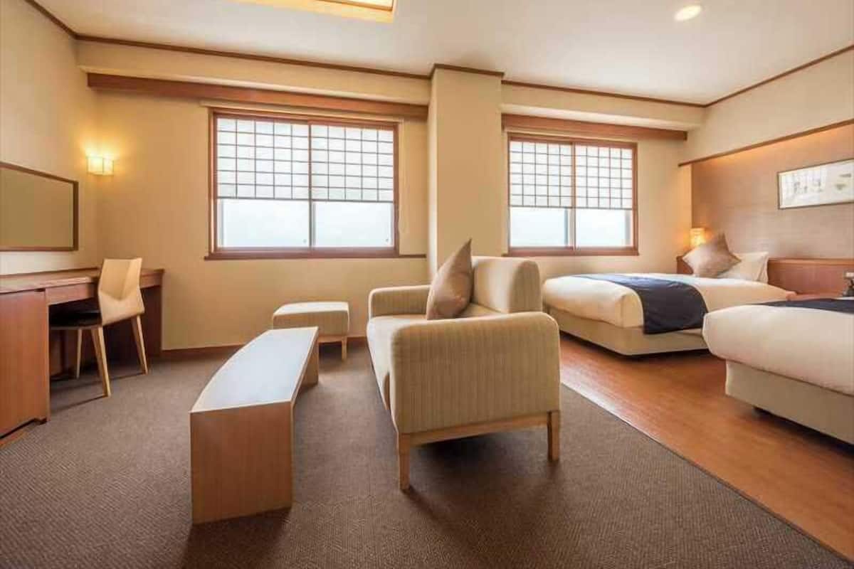 A hotel room with a desk, two sofas, a bench, and large windows.