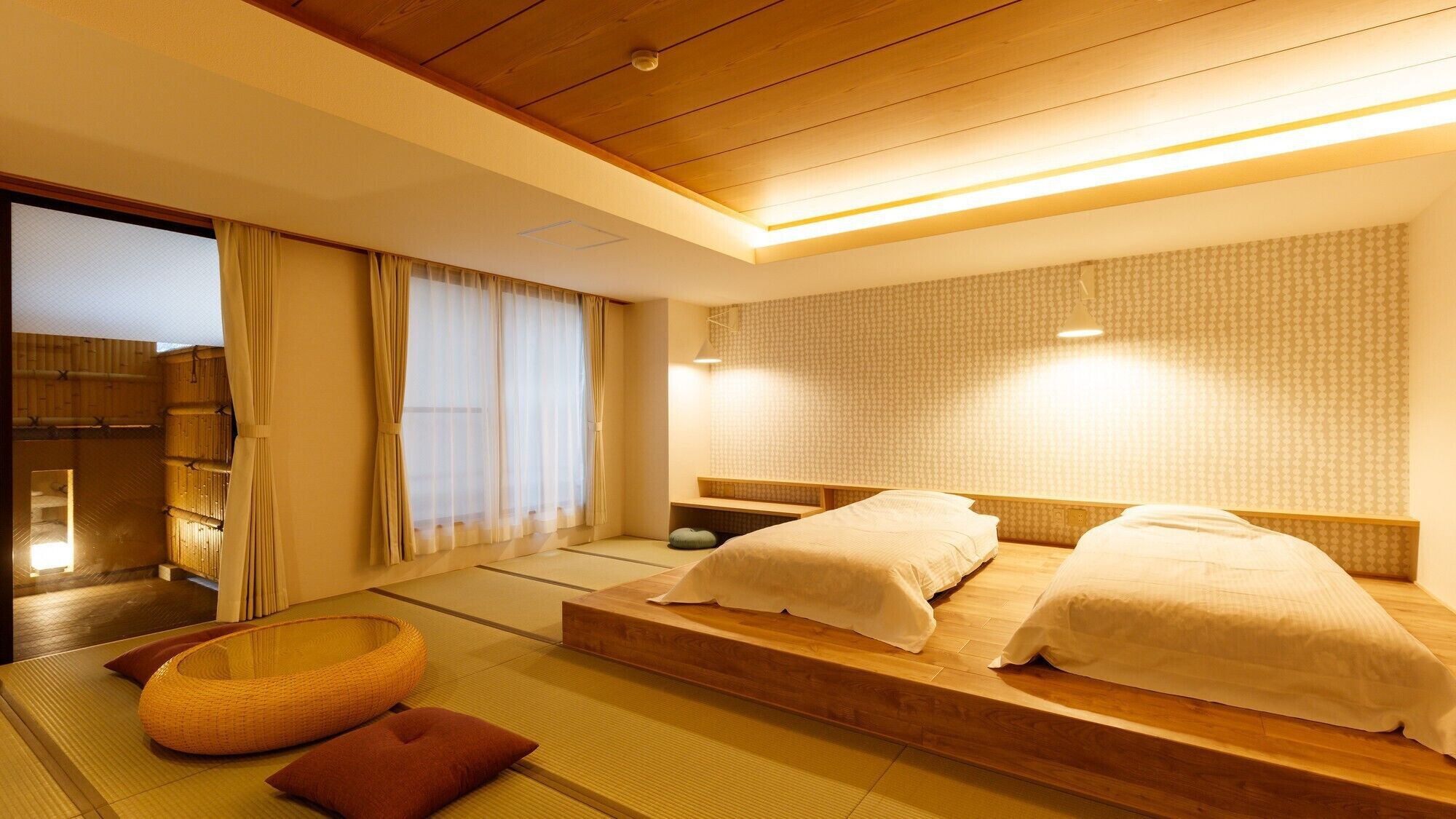A traditional Japanese-style room with tatami flooring, a low wooden bed with white bedding, a futon, a woven basket, and a sliding door leading to a bathroom.
