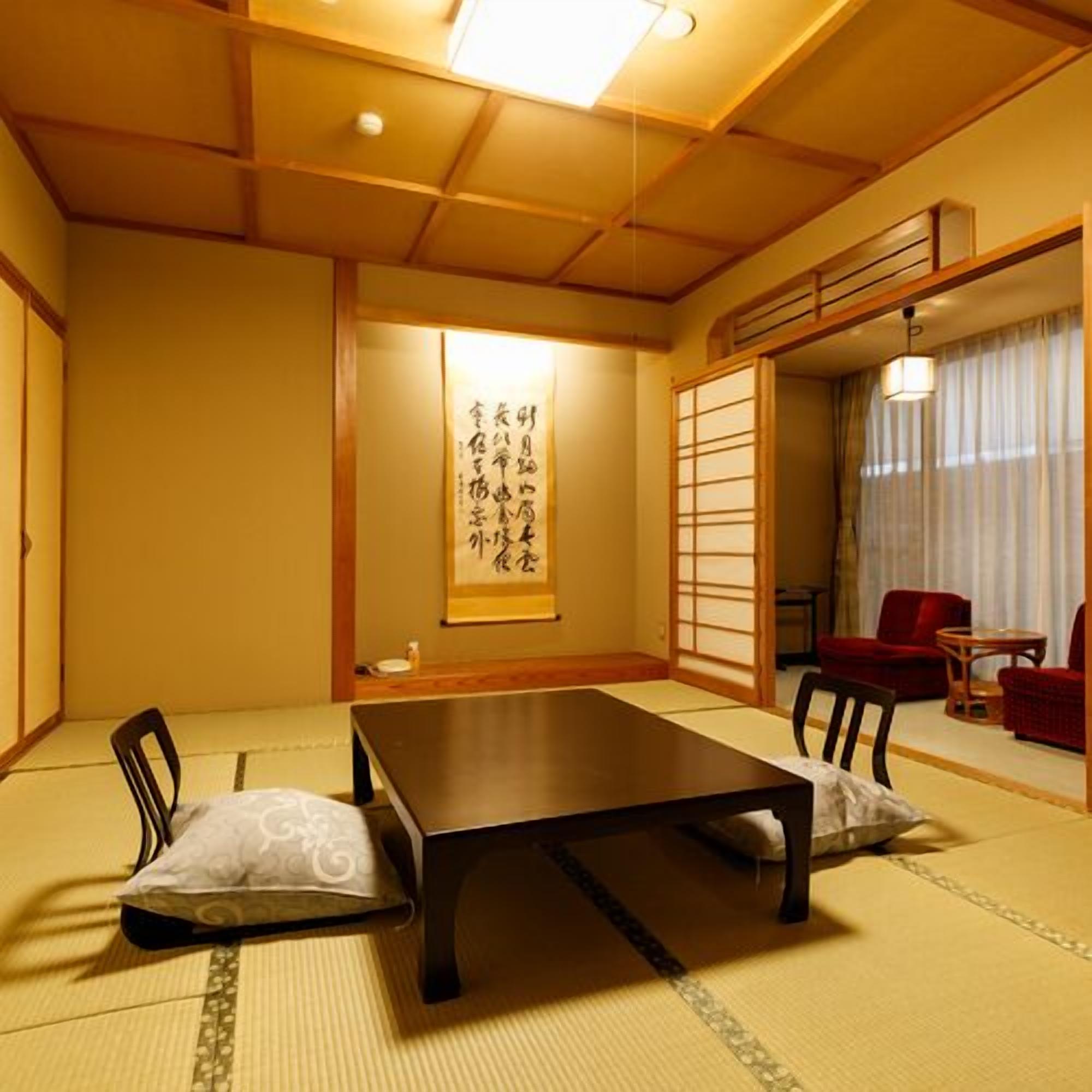 A traditional Japanese room with tatami flooring, a low table, and red chairs.