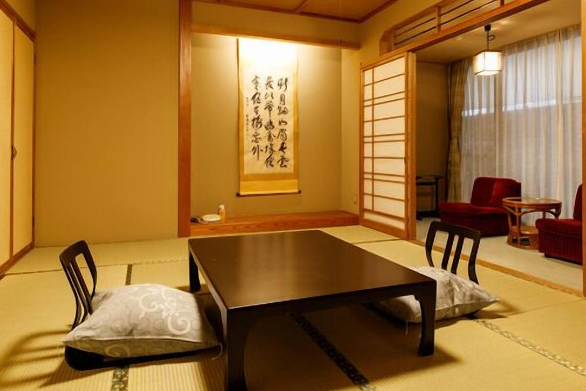 A traditional Japanese room with tatami flooring, a low table, and red chairs.