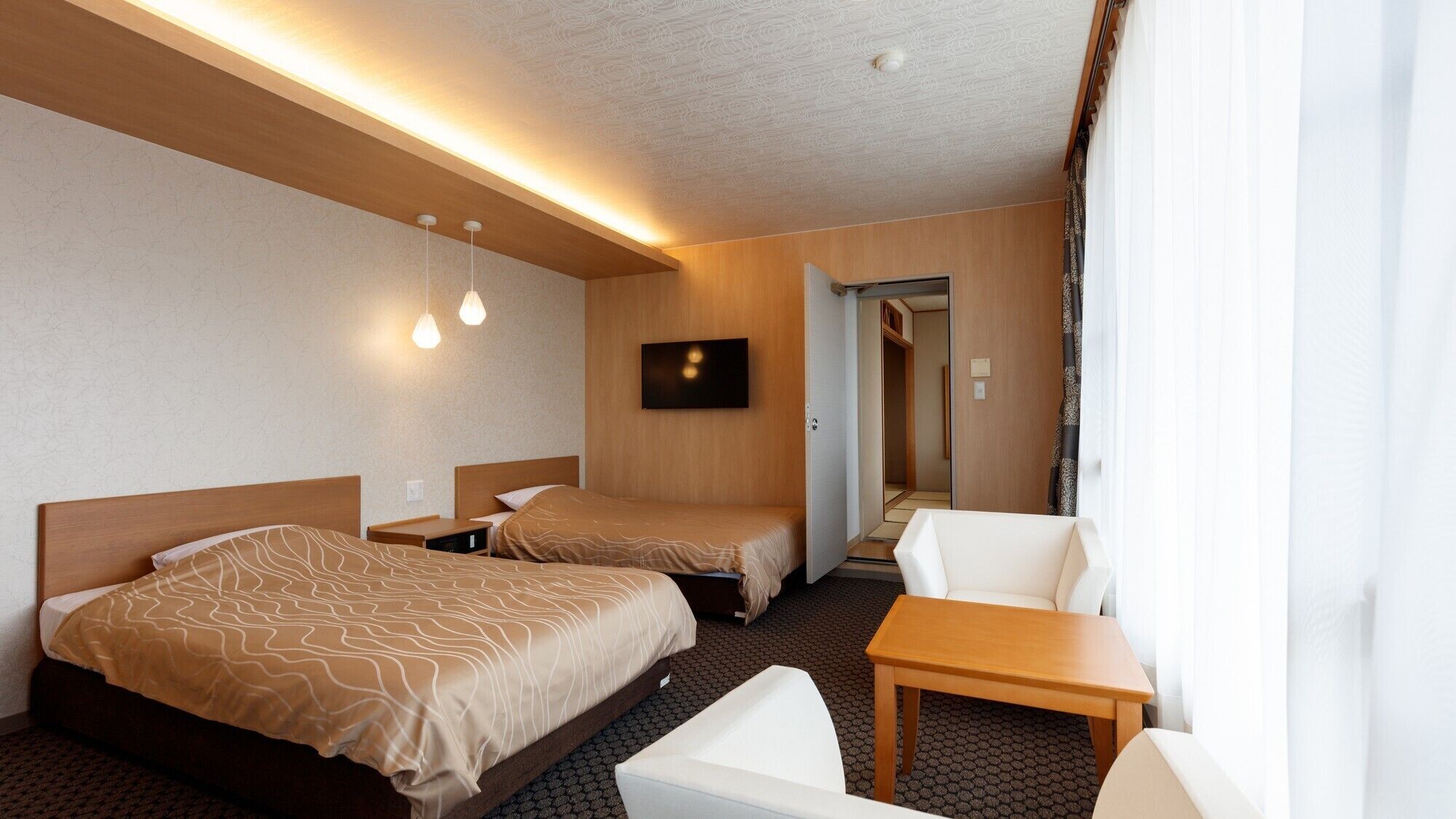 A hotel room with two beds, a TV, a small table, and a chair.
