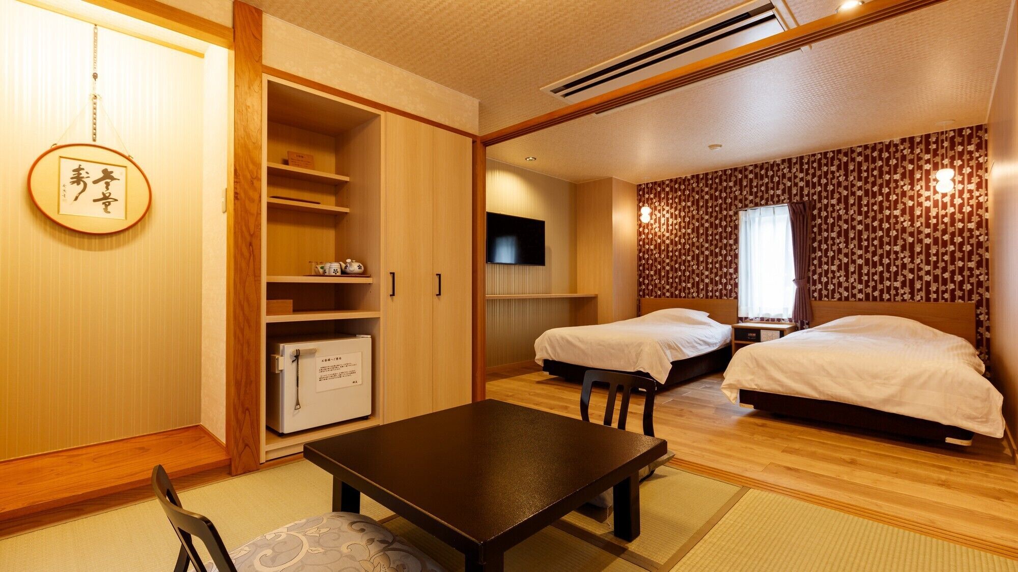 A traditional Japanese-style room with two beds, a TV, a small table, and a wardrobe.