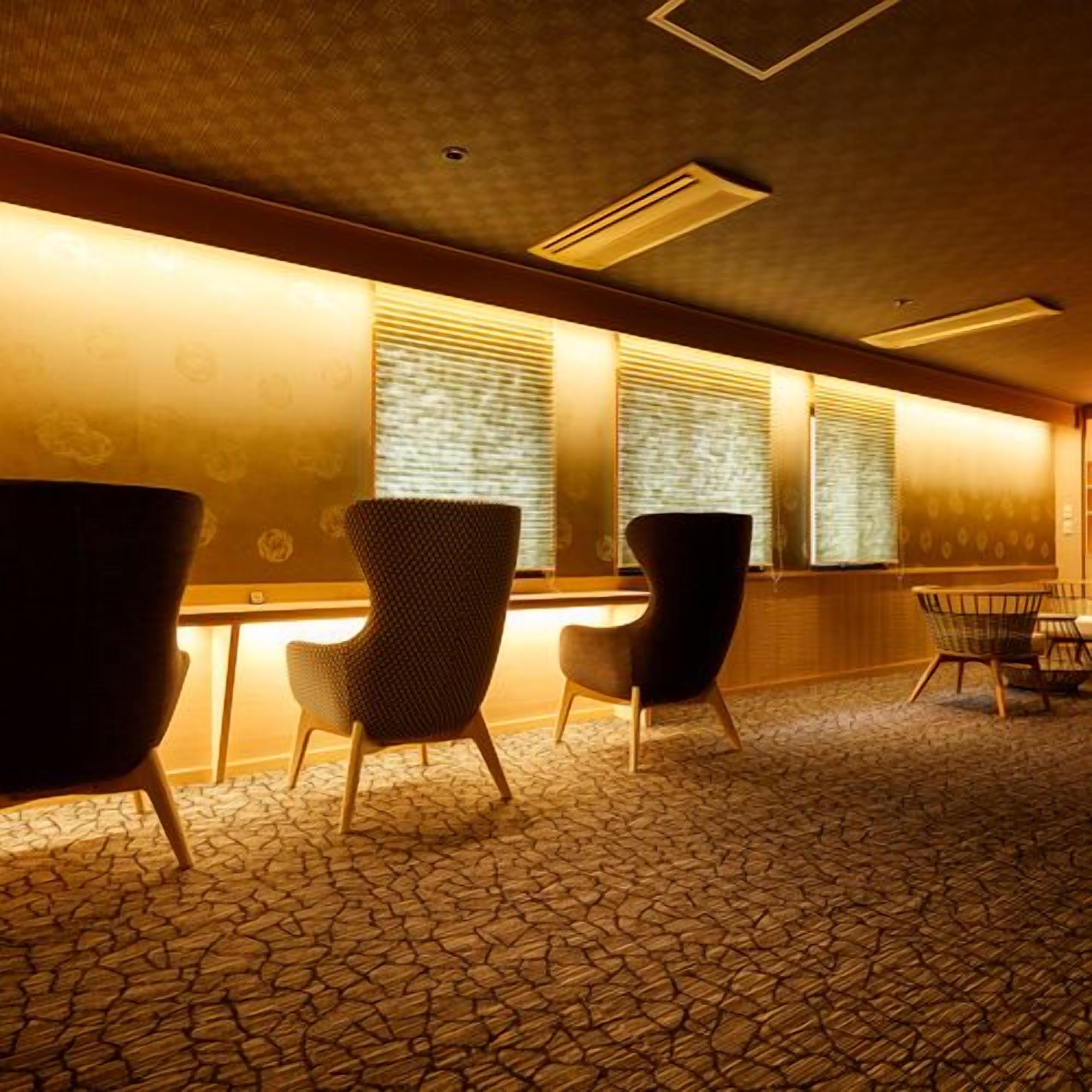 A waiting area with patterned carpet, two upholstered chairs, a small table, and a window with blinds.