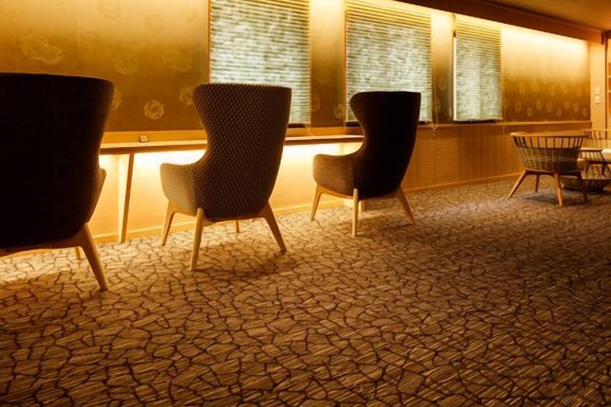 A waiting area with patterned carpet, two upholstered chairs, a small table, and a window with blinds.