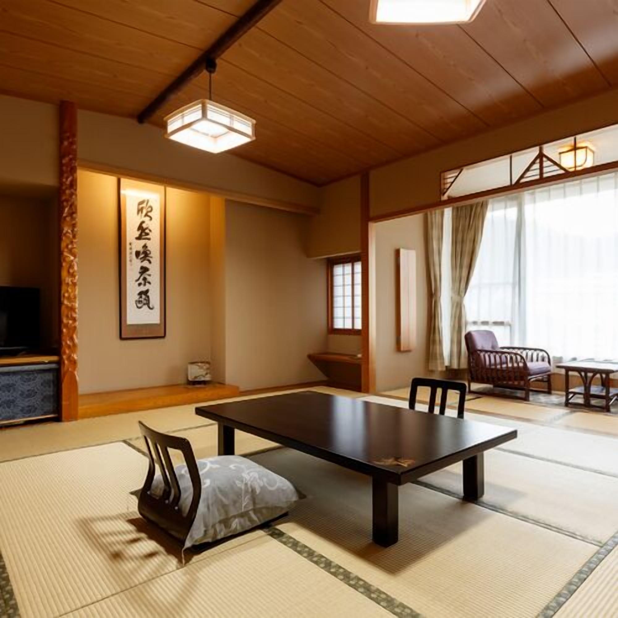 Una habitación japonesa tradicional con suelo de tatami, una mesita baja, sillas y un televisor.