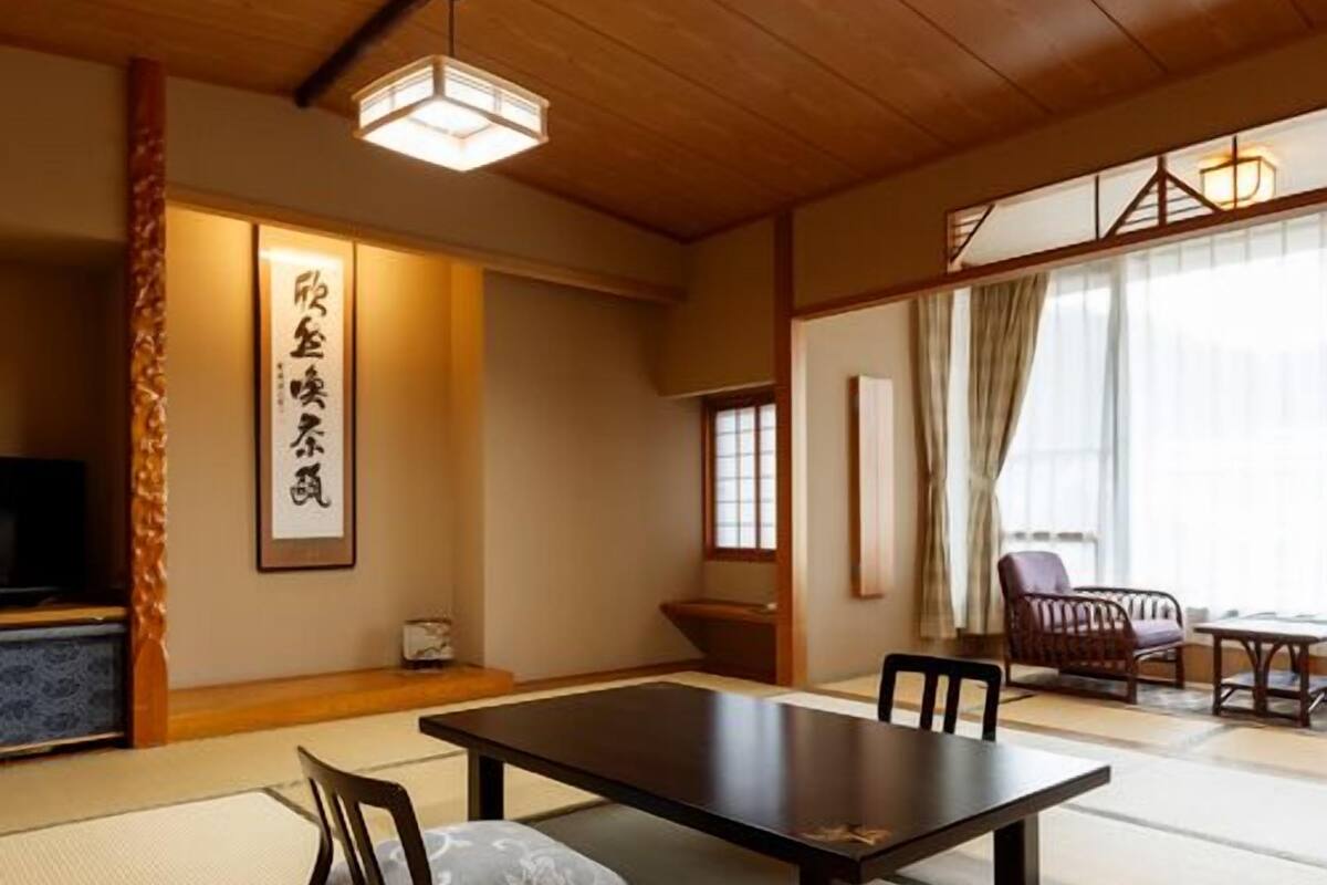 A traditional Japanese room with tatami flooring, a low table, chairs, and a television.